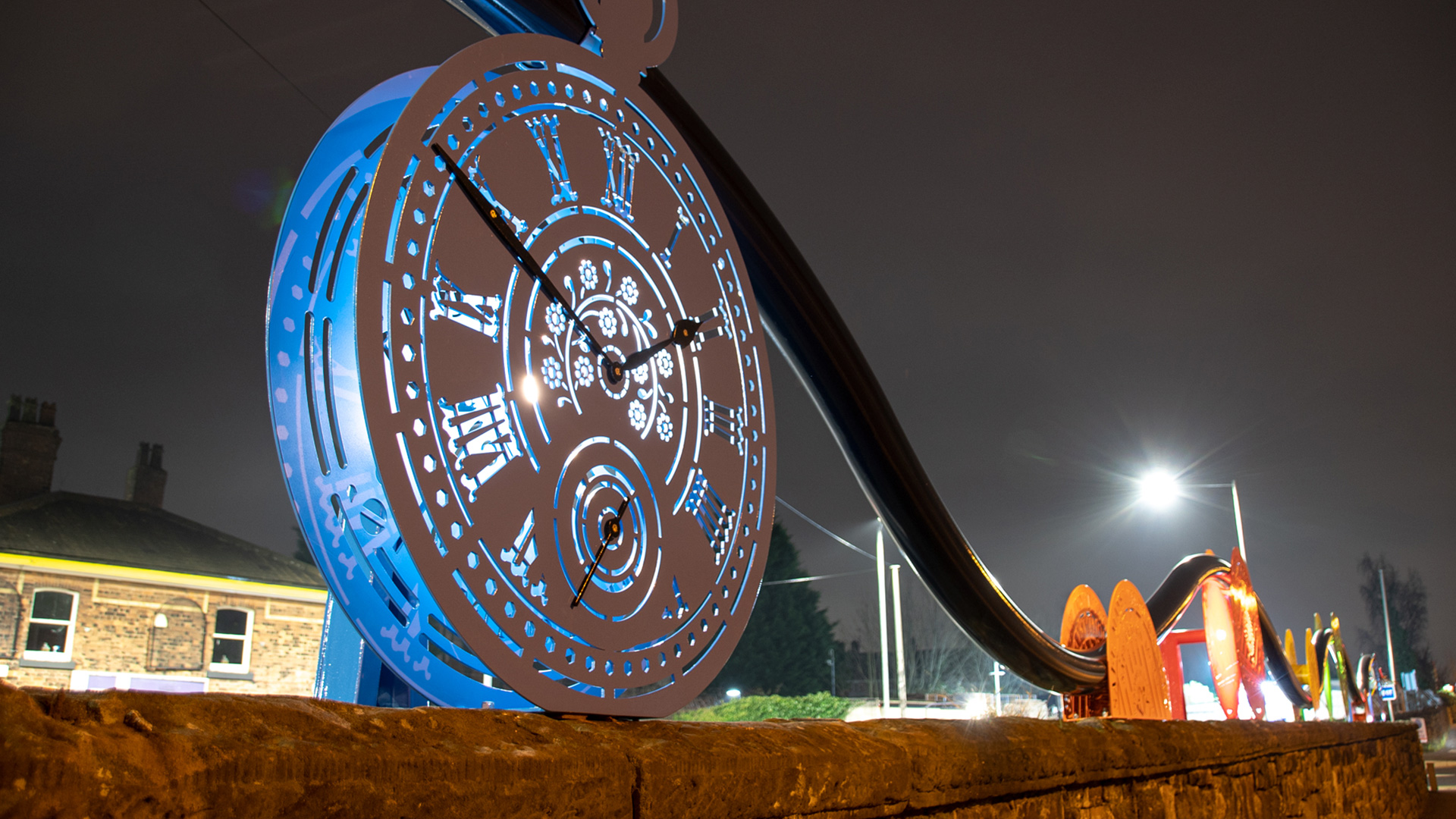 Prescot gateway artwork — backlit pocket-watch face at night